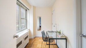 A narrow hallway with a radiator, a glass table with a chair, and a door leading to another room.
