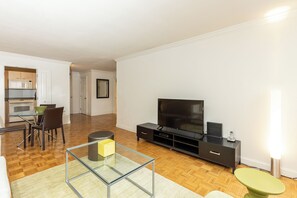 A modern living room with a flat-screen TV, a glass coffee table, and a dining area with chairs and a table.