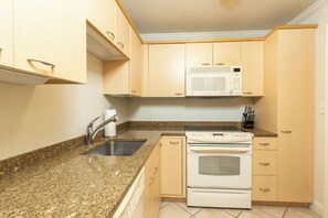 A kitchen with granite countertops, a stainless steel sink, a white microwave, and a double oven.
