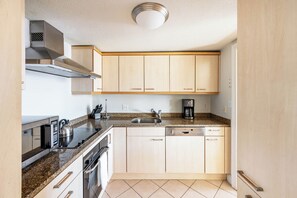A compact kitchen with a microwave, stove, sink, and coffee maker.