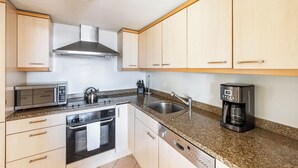 Una cocina con armarios de madera, campana extractora de acero inoxidable, microondas, hervidor, cafetera y lavavajillas.