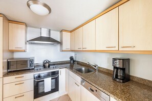 A kitchen with wooden cabinets, a stainless steel range hood, a microwave, a kettle, a coffee maker, and a dishwasher.
