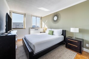 A modern hotel room with a large bed, a desk, a TV, and a city view.