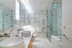 A modern bathroom with a large mirror, two sinks, a toilet, and a glass-enclosed shower. - Bright Escape | Fifth Ave | W/D & Gym (New York)