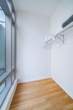 A corner room with a wooden floor, white walls, and a window with a view of buildings.