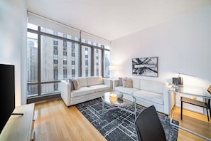 Ein modernes Wohnzimmer mit großem Fenster, zwei weißen Sofas, einem Glastisch und einem schwarzen Teppich.