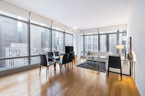 A modern living room with large windows, a dining area, and a sofa.