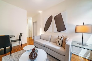 Un salon moderne avec un canapé, une table basse, une lampe et des œuvres d’art abstraites accrochées au mur.