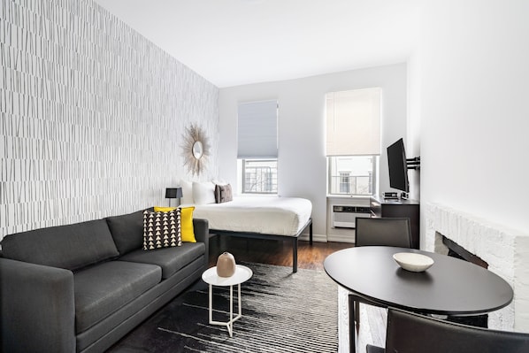 A modern hotel room with a sofa, a small round table, a bed, a TV, and a patterned wall.