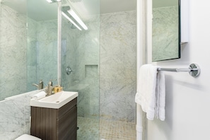 A modern bathroom with a glass shower enclosure, a white sink, and a towel rack.