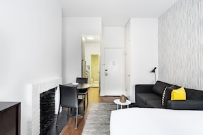 A modern hotel room with a fireplace, a dining area, a sofa, and a patterned wall.