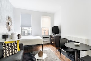 A modern hotel room with a bed, a sofa, a TV, a dining table, and a fireplace.