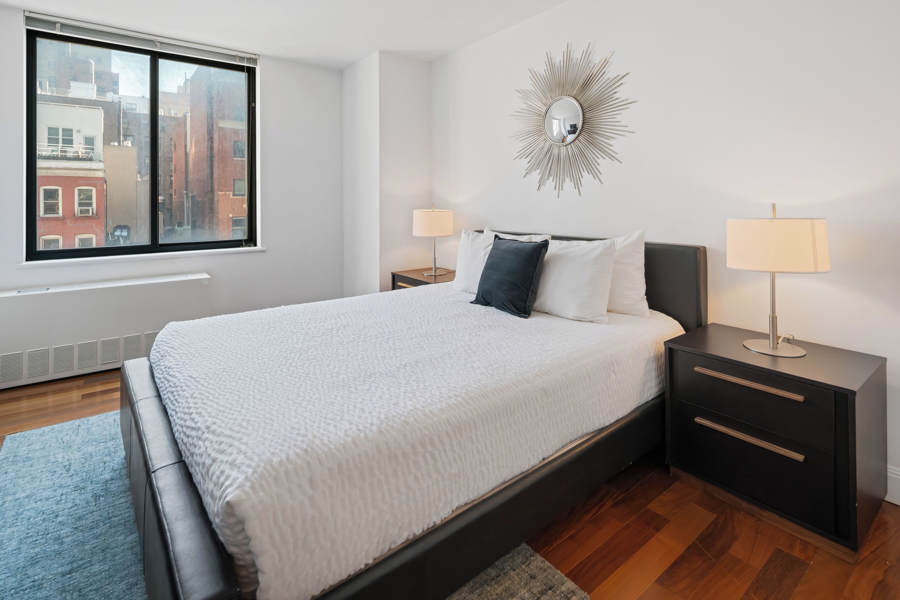 Een keurig opgemaakt slaapkamer met een groot bed, twee nachtkastjes en een uitzicht op de stad door een raam.