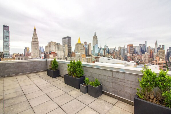 Terraço no telhado com vista para o horizonte da cidade, com edifícios modernos e um campanário.