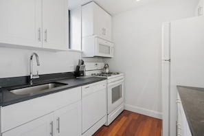 A modern kitchen with white cabinets, a black countertop, a stainless steel sink, a microwave, a stove, and a refrigerator. - Contemporary Gramercy Stay | Balcony, Rooftop Deck (New York)