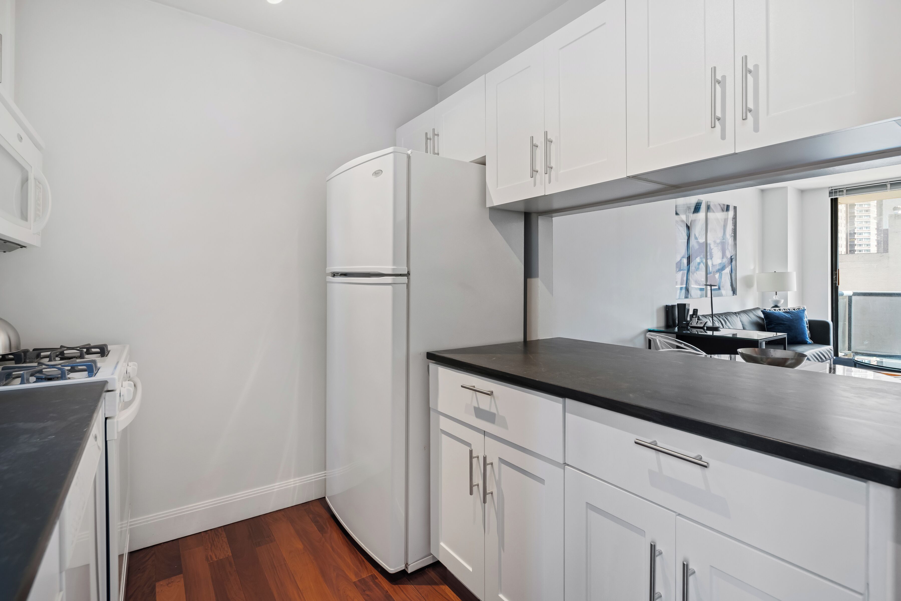 A compact kitchen with white cabinets, a black countertop, and a built-in refrigerator.