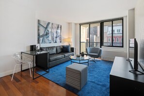 A modern living room with a sofa, a coffee table, a TV, and a large window with a city view. - Contemporary Gramercy Stay | Balcony, Rooftop Deck (New York)