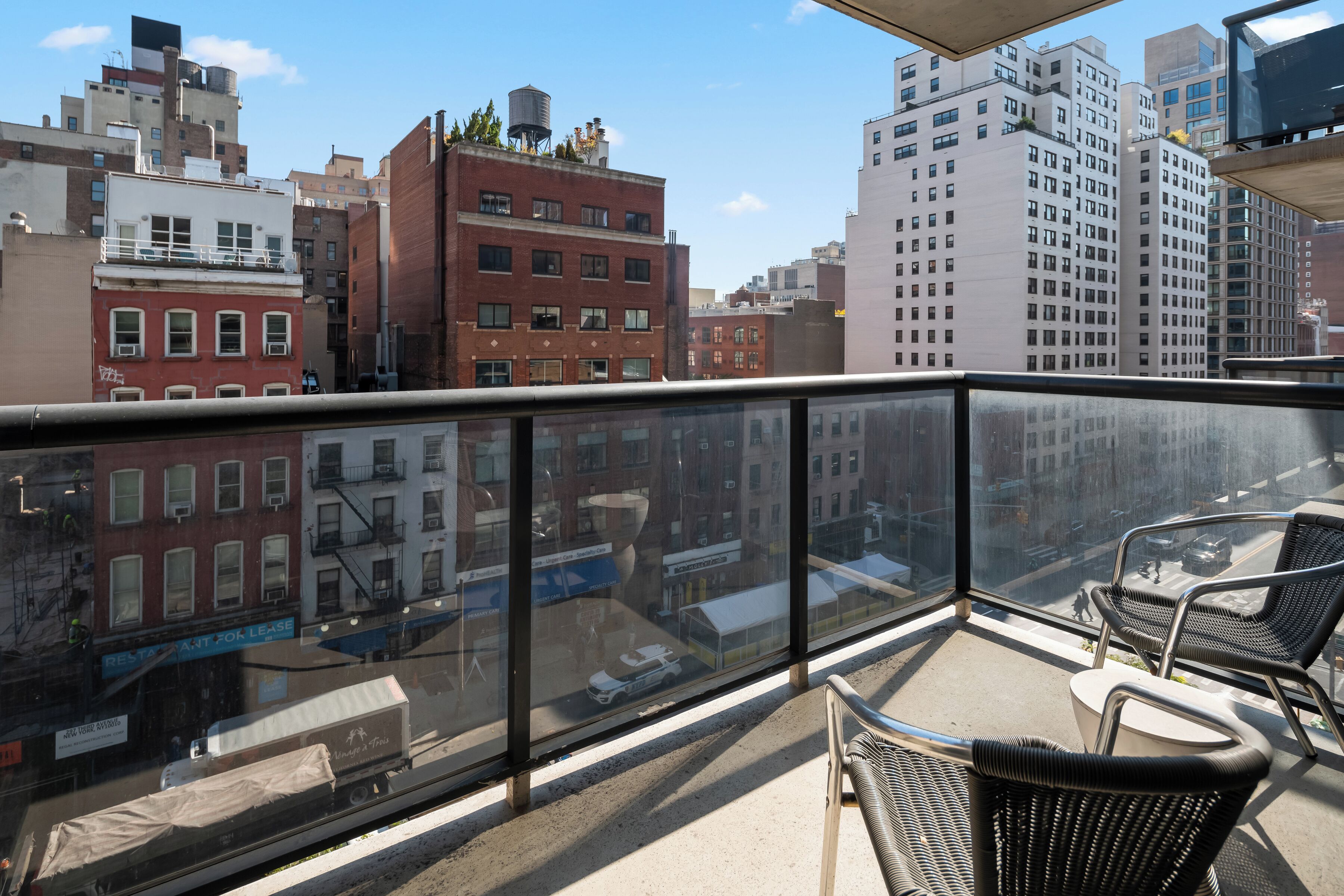 A balcony with wicker chairs, a view of a cityscape with buildings, and a clear sky.