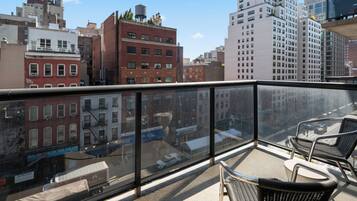 A balcony with wicker chairs, a view of a cityscape with buildings, and a clear sky.