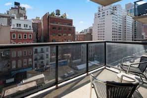 A balcony with wicker chairs, a view of a cityscape with buildings, and a clear sky. - Contemporary Gramercy Stay | Balcony, Rooftop Deck (New York)