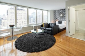 A modern living room with a large window, a black sofa, a glass coffee table, and a black shag rug.