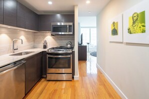 A modern kitchen with stainless steel appliances, wooden flooring, and artwork on the walls.