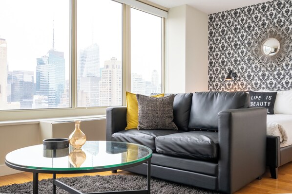 A modern living room with a city view, a glass coffee table, a black leather sofa, and a patterned wallpaper.