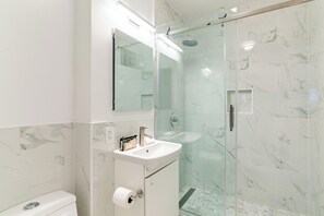 Un baño moderno con ducha de vidrio, un lavamanos blanco y pared con azulejos de mármol.