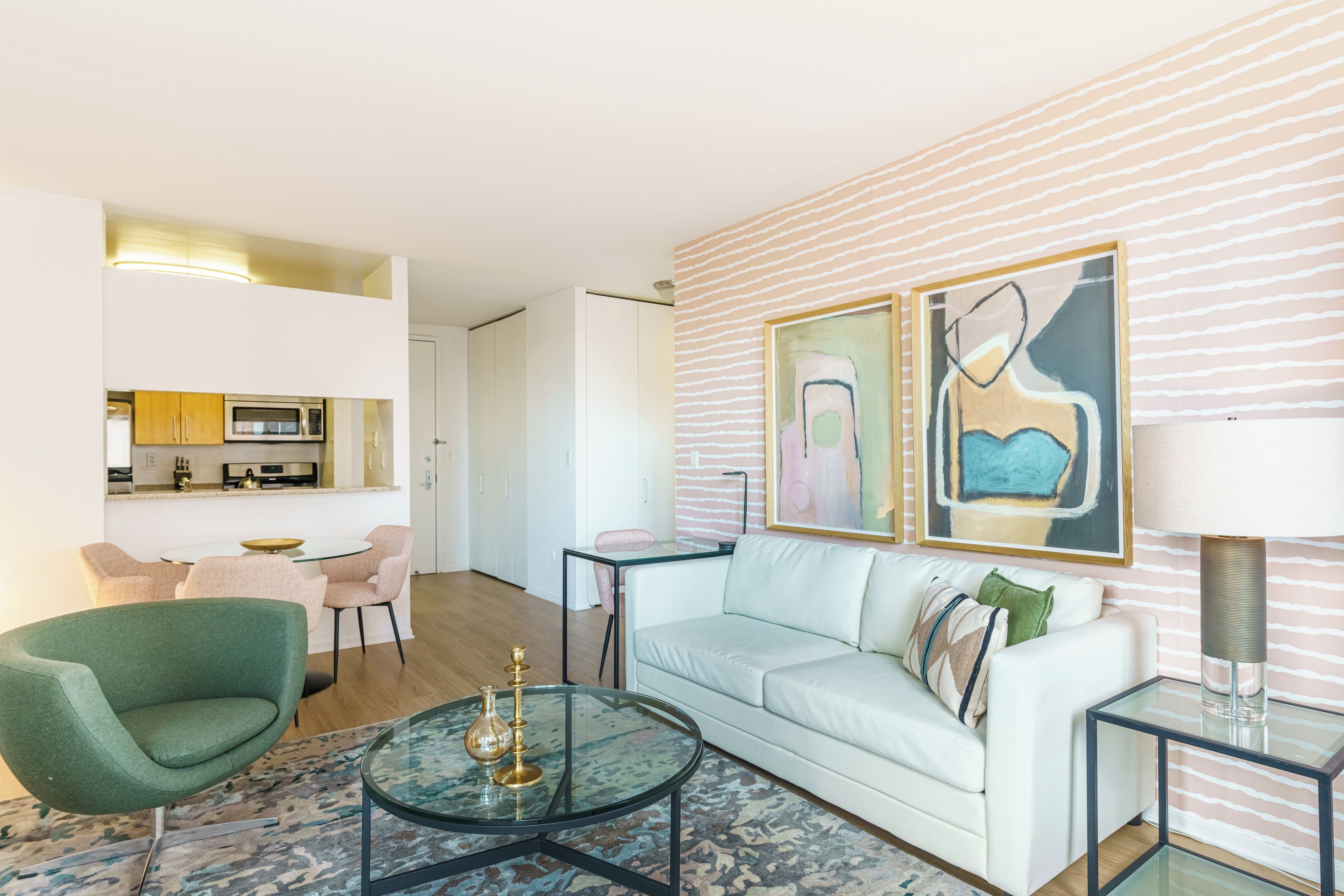 A modern living room with a glass coffee table, a white sofa, and a green armchair. There is a dining area with a table and chairs in the background.
