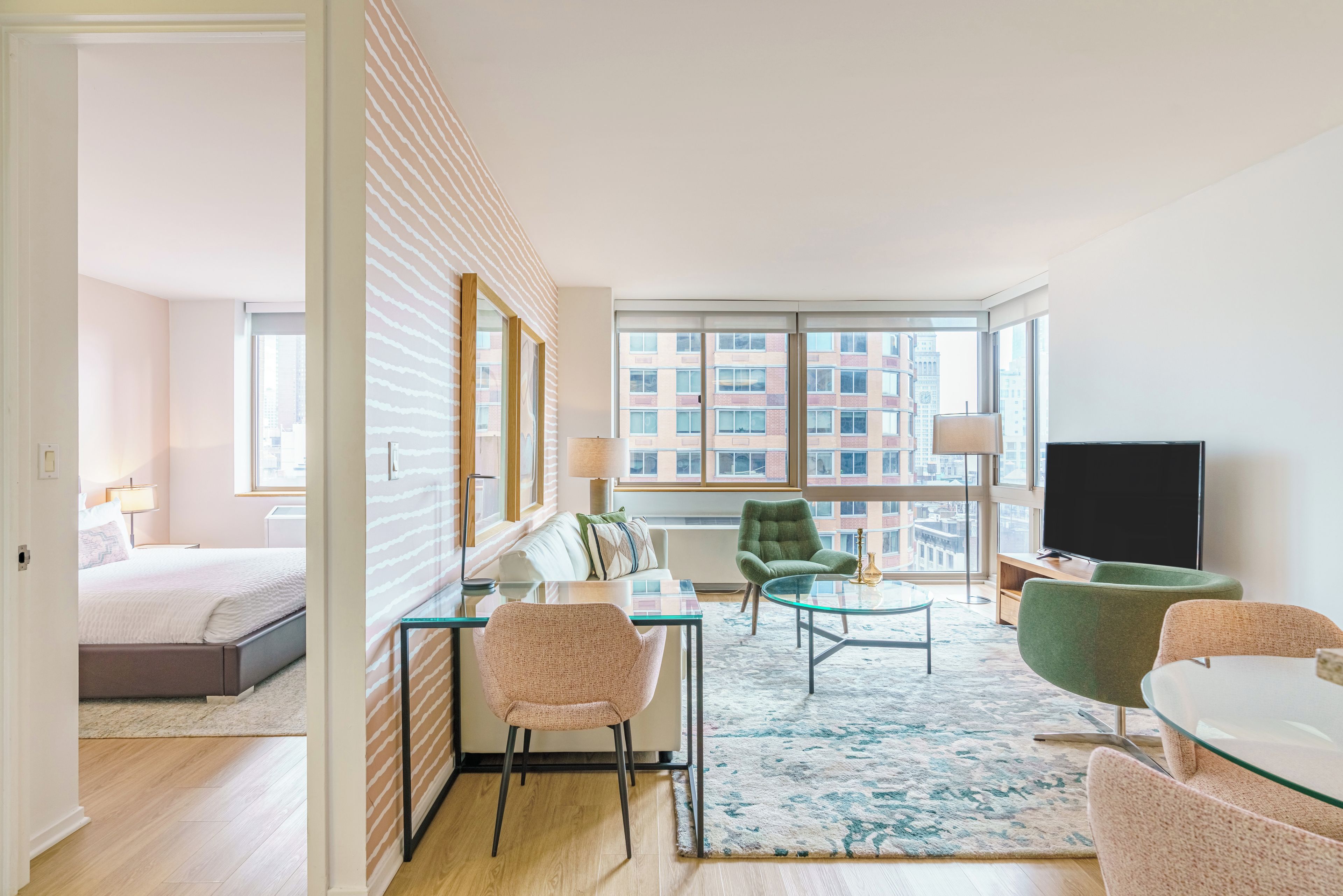 Quarto de hotel moderno com uma janela grande, uma cama, uma mesa de centro de vidro e uma TV.