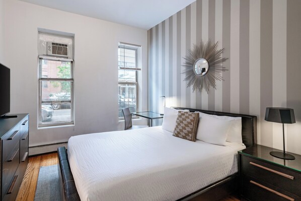 A hotel room with a large bed, a desk, a chair, a TV, and a window with blinds.