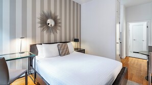 A hotel room with a large bed, a glass desk, a chair, a mirror, and a striped wall. - Near Central Park | Pet-Friendly & Hardwood Floors (New York)