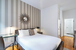 A hotel room with a large bed, a glass desk, a chair, a mirror, and a striped wall.