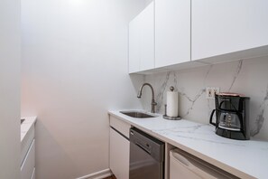 A compact kitchen with white cabinets, a stainless steel sink, a dishwasher, and a coffee maker.