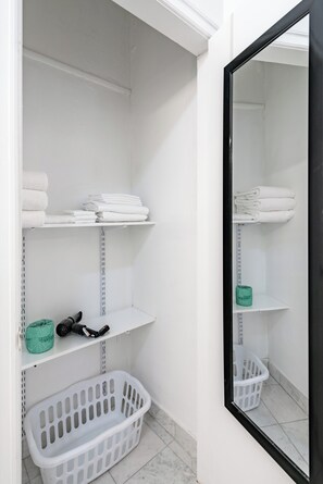 Een schone, witte badkamer met planken met handdoeken en een mand.