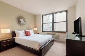 A bedroom with a bed, bedside lamps, a TV, a heater, and a window with blinds. - 1 Bedroom in Jersey City with Luxury Amenities (Jersey City)