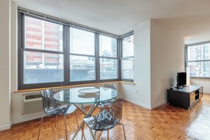 A room with a glass table and chairs, a black entertainment unit, and large windows with a city view. - 1 Bedroom in Jersey City with Luxury Amenities (Jersey City)