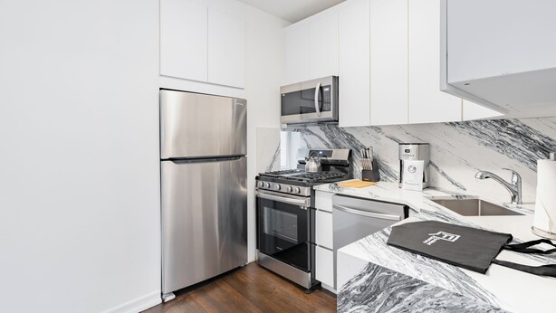 Una cocina compacta con electrodomésticos de acero inoxidable, encimera de mármol y muebles de color blanco.