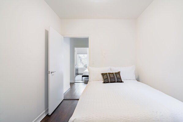 A bedroom with a large bed, a door leading to another room, and a view of a bathroom.