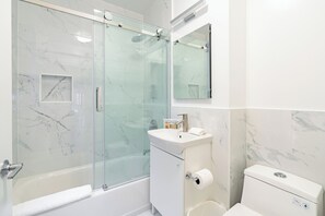 Ein modernes Badezimmer mit einer Duschkabine, einem weißen Waschbecken und einer Toilette.