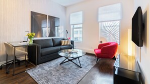 Una sala de estar moderna con un sofá negro, una silla roja, una mesa de centro de vidrio y un televisor montado en la pared.