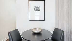 Una habitación moderna con una mesa redonda, dos sillas negras, un cuadro enmarcado en la pared y una cortina con textura.