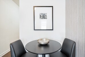 Ein modernes Zimmer mit einem runden Tisch, zwei schwarzen Stühlen, einem gerahmten Bild an der Wand und einem strukturierten Vorhang.