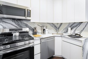 A modern kitchen with white cabinets, a stainless steel stove, a microwave, and a marble backsplash. - Charming Two Bedroom Conveniently Located on UES (New York)