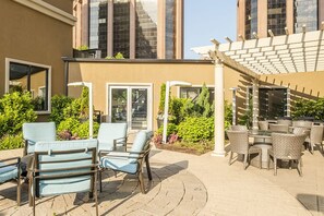 An outdoor patio area with lounge chairs and tables, surrounded by greenery and a building with large windows. - 2 Bedroom Steps from Metro-North to NYC (White Plains)