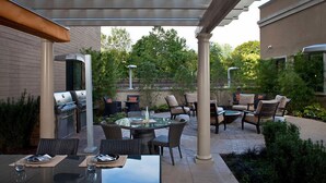 Un patio al aire libre con pérgola, mobiliario, una parrilla y una mesa redonda.