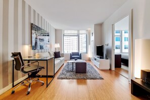 Ein modernes Wohnzimmer mit einer Couch, einem Glastisch, einem Sessel, einem Fernseher und einem großen Fenster mit Blick auf die Stadt.