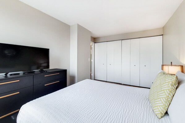 A bedroom with a bed, a TV on a dresser, a wardrobe, and a bedside lamp.