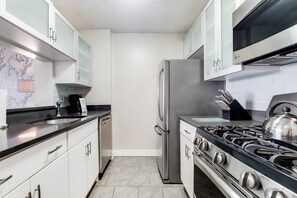 Eine Küche mit weißen Schränken, einem Edelstahlkühlschrank, einem Gasherd und einer Mikrowelle.
