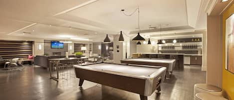 A spacious room with a pool table, bar area, and seating.